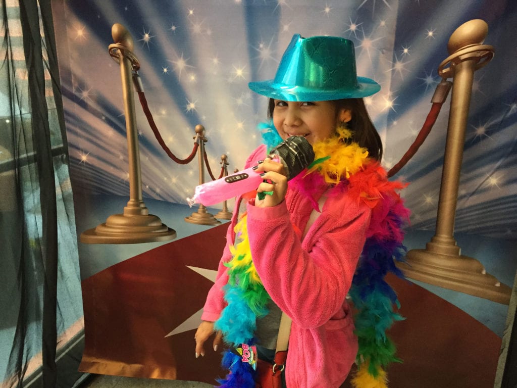a girl with a hat on and a colorful boa holding an inflatable toy microphone