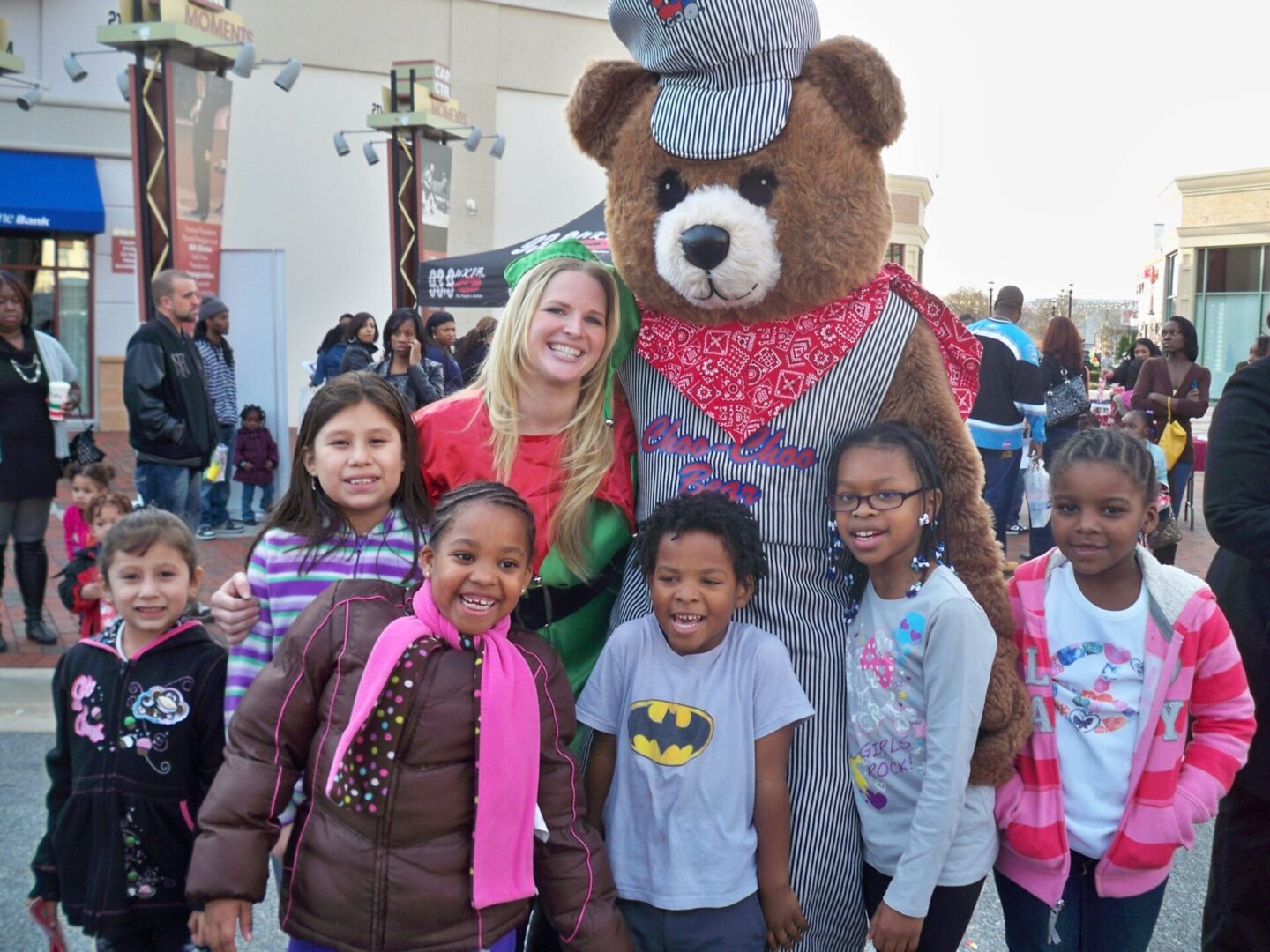 a bear mascot posing with a woman and a group of kids
