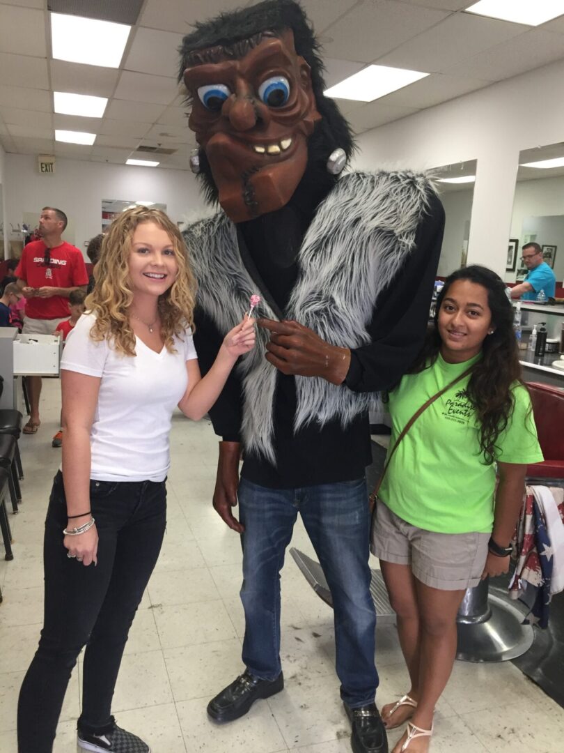 two girls posing with a Frankenstein mascot